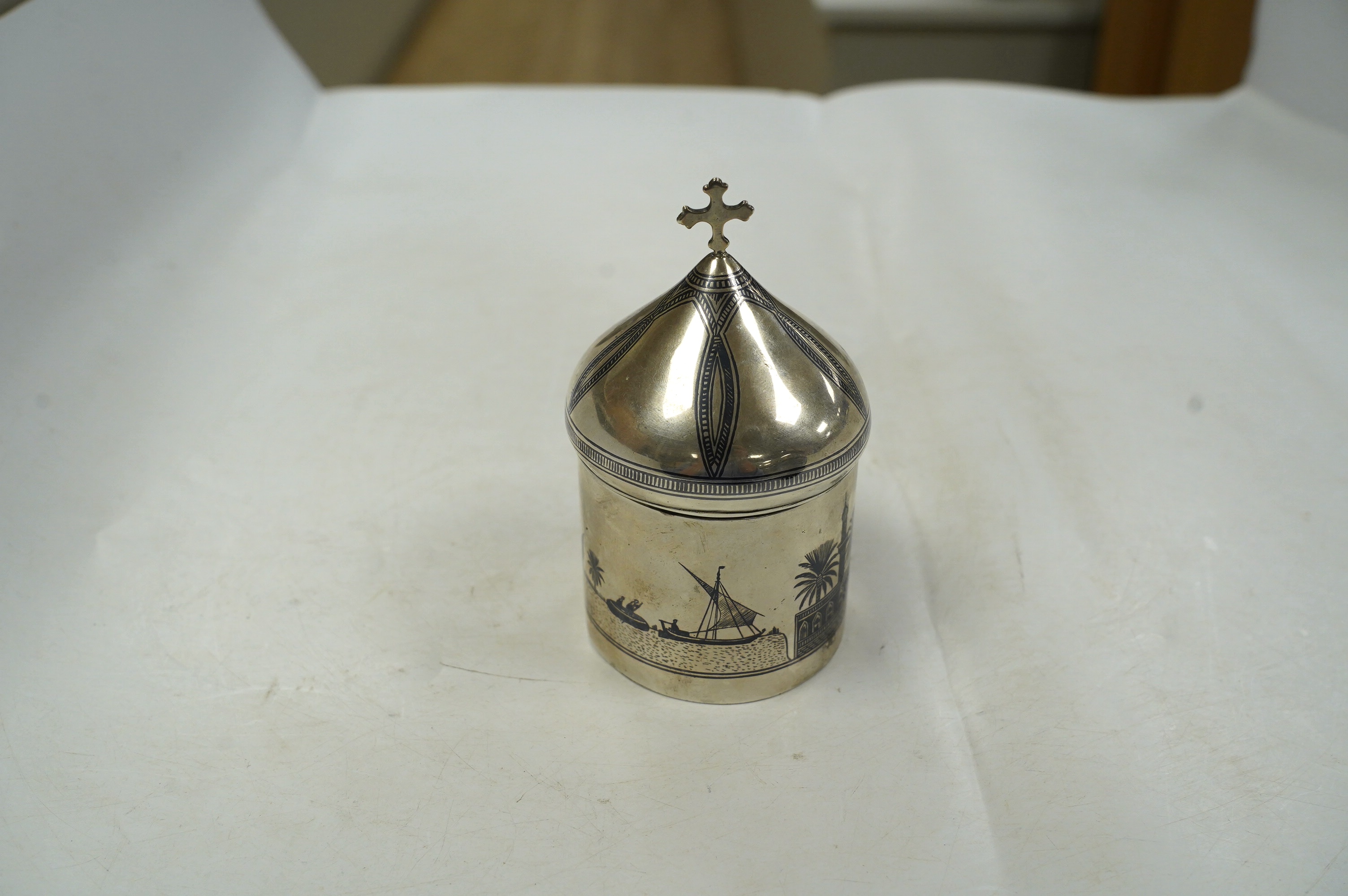 A Middle Eastern white metal and niello box and cover, with cross finial, 11.8cm, gross weight 4.4oz. Condition - poor to fair